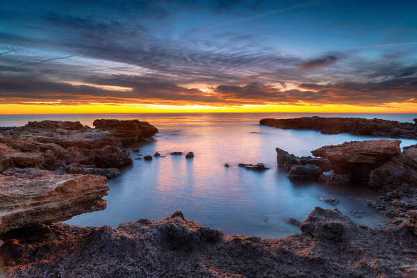 Beautiful sunrise over rocks at the beach at Torre de la Sal Picture Board by Helen Hotson
