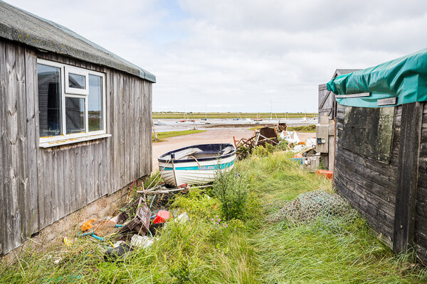 Fishing boat between fishing huts at Brancaster Staithe Picture Board by Jason Wells