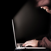 Buy canvas prints of Hooded computer hacker using laptop by Simon Bratt LRPS