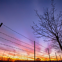 Buy canvas prints of Fiery sunset viewed through barbed fence by Simon Bratt LRPS