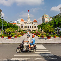 Buy canvas prints of A motorcyclist rides along the road.past a statue of Ho Chi Minh by Kevin Hellon