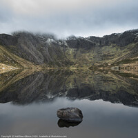 Buy canvas prints of Beautiful moody Winter landscape image of Llyn Idwal and snowcapped Glyders Mountain Range in Snowdonia by Matthew Gibson