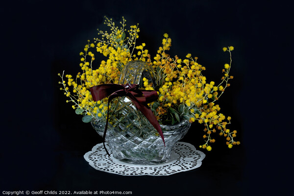 Wattle blossoms in a crystal glass basket vase on black. Wattle  Picture Board by Geoff Childs