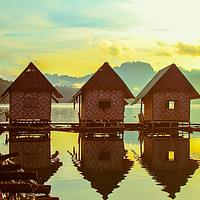 Buy canvas prints of Sun rising over cute little wooden huts perched on by  