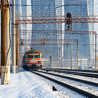 Buy canvas prints of An electric train moves on rails against the backdrop of a cityscape of skyscrapers in a winter haze. by Sergii Petruk