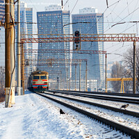 Buy canvas prints of An old electric train moves on rails against the backdrop of a cityscape of skyscrapers on a sunny winter day. by Sergii Petruk