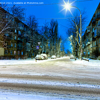 Buy canvas prints of Snow-covered intersection on the road along a city street with trees in the snow and evening city illumination against the background of blue twilight. by Sergii Petruk