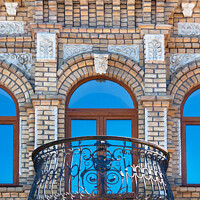 Buy canvas prints of Arched windows with a beautiful, expressive balcony on the brick facade of the old house and the reflection of the blue sky in the glass windows. by Sergii Petruk