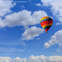Buy canvas prints of A motley multicolored hot air balloon raises a basket with tourists in the blue sky among white clouds. by Sergii Petruk