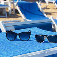 Buy canvas prints of A pair of sunglasses lie on a blue sun lounger under the sun on a summer day. by Sergii Petruk