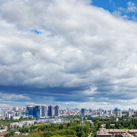 Buy canvas prints of A large white and gray cloud loomed over a green park in the old residential area of the city and new buildings on the horizon against the backdrop of a bright summer day. by Sergii Petruk