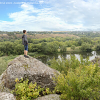 Buy canvas prints of The teenager stands on top of a large stone boulder on the bank of the Southern Bug River and looks at the river below by Sergii Petruk