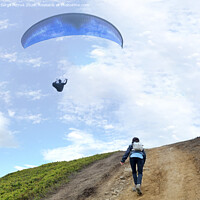 Buy canvas prints of A young woman climbs up a mountain to meet a paraglider hovering in the air by Sergii Petruk