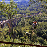 Buy canvas prints of A tourist crosses over a long cable car over a mountain and a forest across the Tiara River. by Sergii Petruk