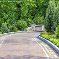 Buy canvas prints of Walkway paved with tiles in a beautiful park, framed by different bushes and flowers, in soft rays of morning light. by Sergii Petruk