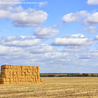 Buy canvas prints of A large stack of straw against the background of a wide field and blue cloudy sky after harvest. by Sergii Petruk
