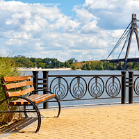 Buy canvas prints of A wooden bench on the embankment of the Dnipro River against the background of yellow paving slabs and the northern bridge over the river in blur. by Sergii Petruk