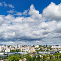 Buy canvas prints of An urban landscape with a green park, residential areas and a TV tower against a bright blue sky with thickening clouds. by Sergii Petruk