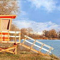 Buy canvas prints of On the bank of the river with bare autumn bushes without leaves stands a lonely wooden house of lifeguards and is illuminated by the rays of the bright autumn sun. by Sergii Petruk