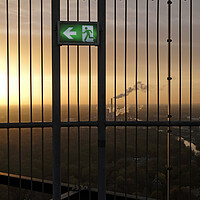 Buy canvas prints of An emergency exit sign with an industrial site in the background by Lensw0rld 