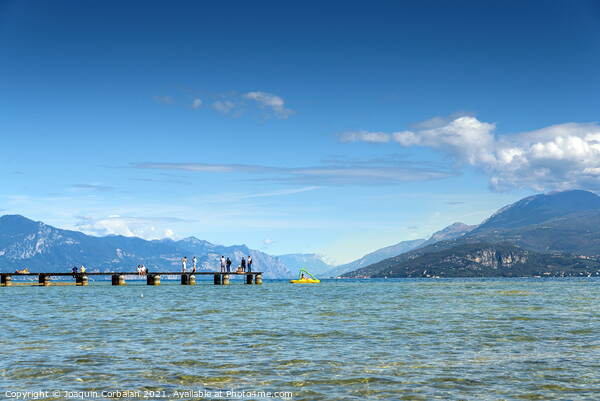 Calm water lake in Garda, Italy with a wooden walkway on a sunny Picture Board by Joaquin Corbalan
