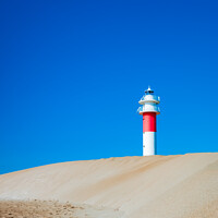 Buy canvas prints of A lighthouse seen from the sand dunes of a beach on a sunny day. by Joaquin Corbalan