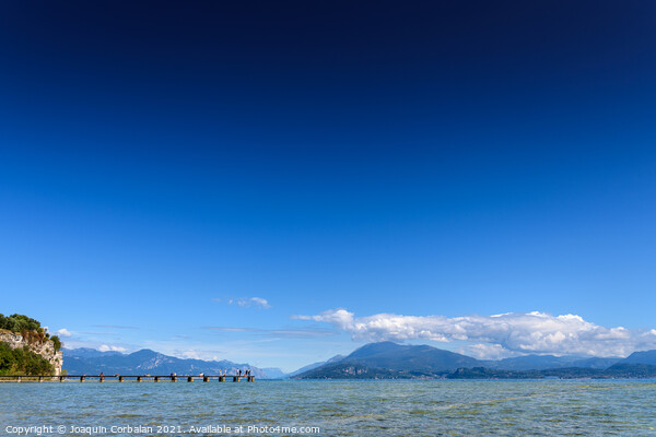 Calm water lake in Garda, Italy with a wooden walkway on a sunny Picture Board by Joaquin Corbalan