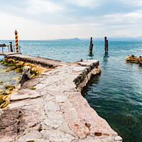 Buy canvas prints of Old stone jetty at the tip of San Vigilio, on Lago di Garda with colorful mooring poles on by Joaquin Corbalan