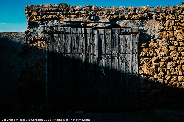 Old and decrepit wooden gate, half lit by the sun, in an unpopul Picture Board by Joaquin Corbalan