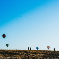 Buy canvas prints of Silhouettes of tourists walking through a meadow while watching hot air balloons flying on the horizon, blue sky background, copy space, added film grain. by Joaquin Corbalan