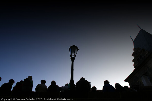  A crowd of tourists rests at dusk on a bridge, silhouetted images backlight against a streetlight. Picture Board by Joaquin Corbalan