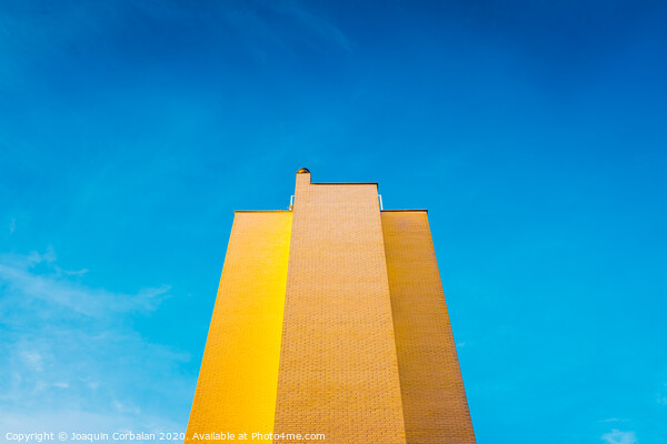 High brick building, warm and yellow at sunset, with the background of an intense blue sky and copy space, minimalist architecture. Picture Board by Joaquin Corbalan