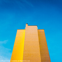 Buy canvas prints of High brick building, warm and yellow at sunset, with the background of an intense blue sky and copy space, minimalist architecture. by Joaquin Corbalan