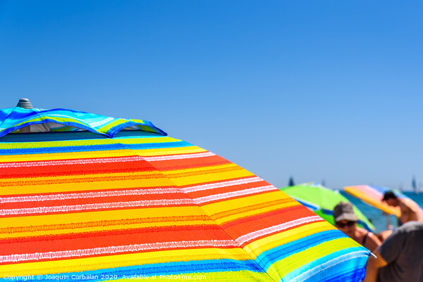 Colorful beach umbrella stuck in the sand surrounded by a group of bathers in summer, near the Mediterranean sea. Picture Board by Joaquin Corbalan