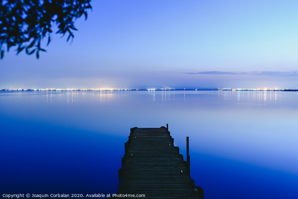 Pier on a lake at sunset with calm water and reflections of relaxing lights. Picture Board by Joaquin Corbalan