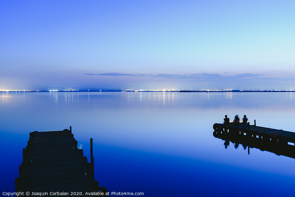 People resting relaxed on a pier on a lake at sunset with calm water Picture Board by Joaquin Corbalan