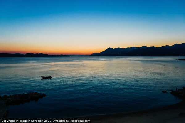 Sunset in a bay with mountains in the background and a small boat anchored. Picture Board by Joaquin Corbalan