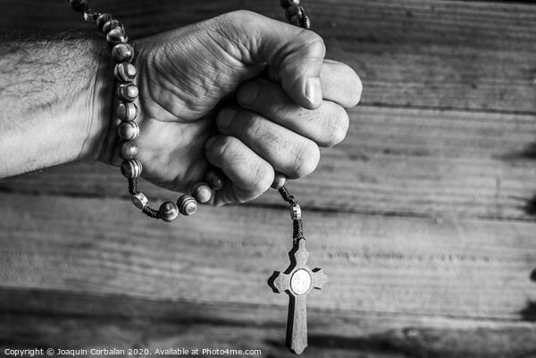 Hand of a religious person holds a Christian rosary during his prayers, unfocused background of woods in black and white. Picture Board by Joaquin Corbalan