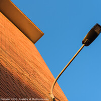 Buy canvas prints of A deep red brick wall supports a lamppost, contrasting and bright colors. by Joaquin Corbalan
