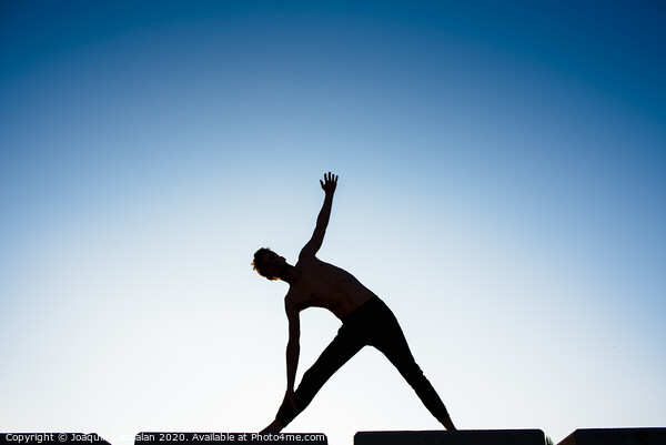 Silhouette of a man practicing yoga, isolated against the blue sky. Picture Board by Joaquin Corbalan