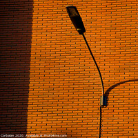 Buy canvas prints of A deep red brick wall supports a lamppost, contrasting and bright colors. by Joaquin Corbalan