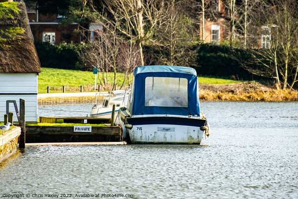 A small boat moored alongside a wooden boat house with a thatched roof on the River Bure in Coltishall, Norfolk Broads Picture Board by Chris Yaxley