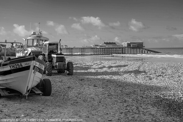 Black and white vintage photo of fishing boats and equipment on Cromer beach on the North Norfolk Coast. In the distance is the Victorian era pier Picture Board by Chris Yaxley