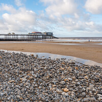Buy canvas prints of View across a sand and shingle beach with a distant pier in the background by Chris Yaxley