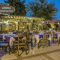 Buy canvas prints of illuminated greek taverna with tables and chairs i by Stig Alenäs