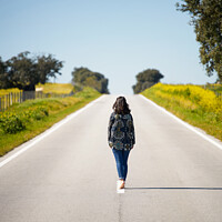Buy canvas prints of Woman walking on the middle of a road in beautiful yellow flowers landscape in Alentejo, Portugal by Luis Pina