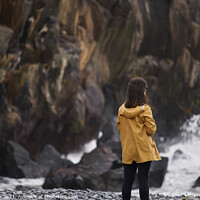 Buy canvas prints of Woman on a yellow rain jacket looking to the sea with rocks on the background, in Madeira by Luis Pina