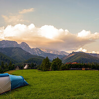 Buy canvas prints of Camping tent put up on green grass meadow field against tatra mountains landscape during sunset sunrise and dramatic clouds, adventure in wild nature concept. by Arpan Bhatia