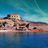 Buy canvas prints of Crete, Greece: Wide angle view of Spinalonga unhabited island with a 16th century venetian fortress and the ruins of a formar leper colony against cloudy blue sky and blue water in the foreground by Arpan Bhatia