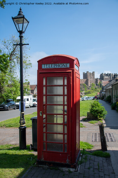 Bamburgh Castle, village and red telephone box Picture Board by Christopher Keeley
